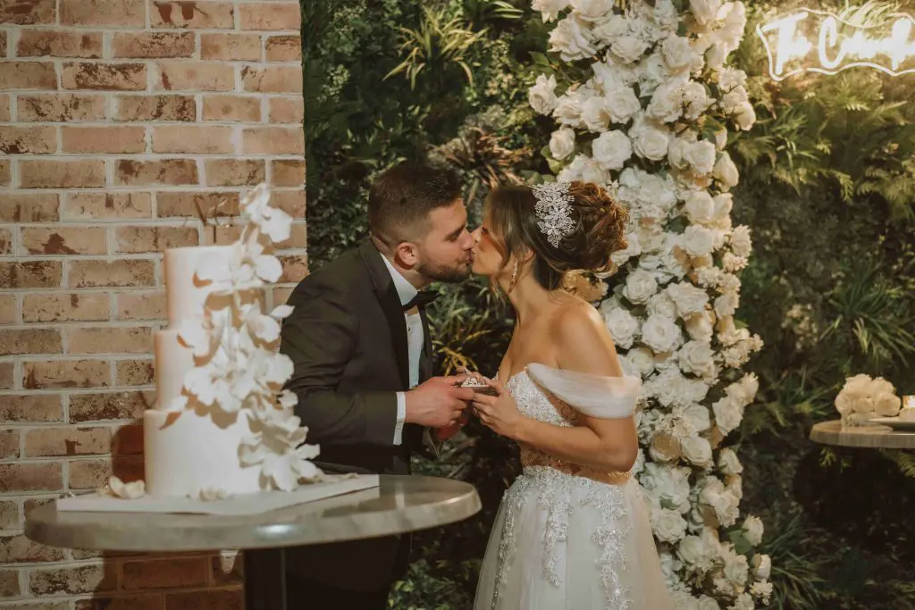 Bride and groom kissing with wedding cake at Perona Farms in Andover, NJ