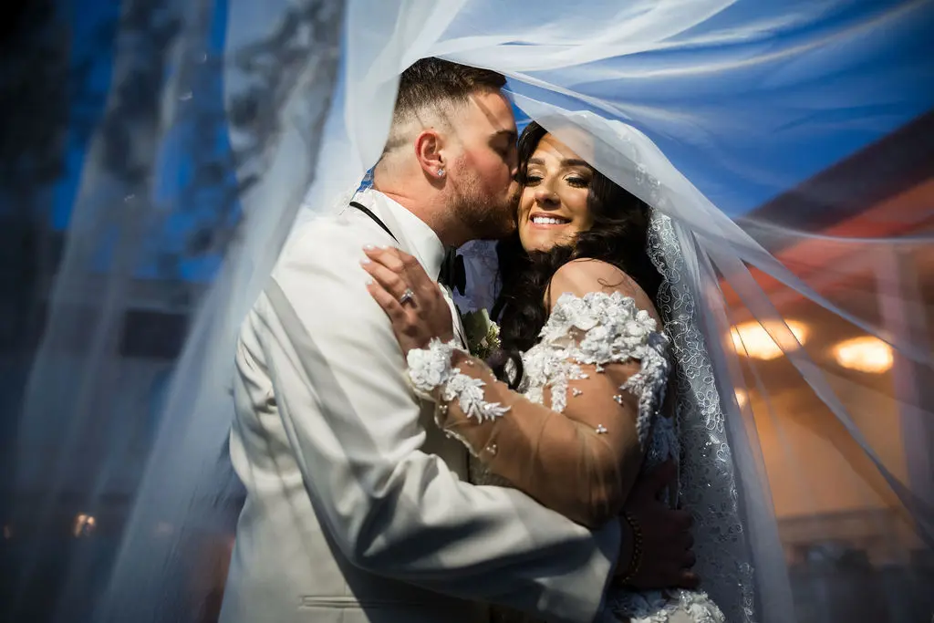 Groom kissing bride with veil over heads at wedding at The Grand in Totowa, NJ
